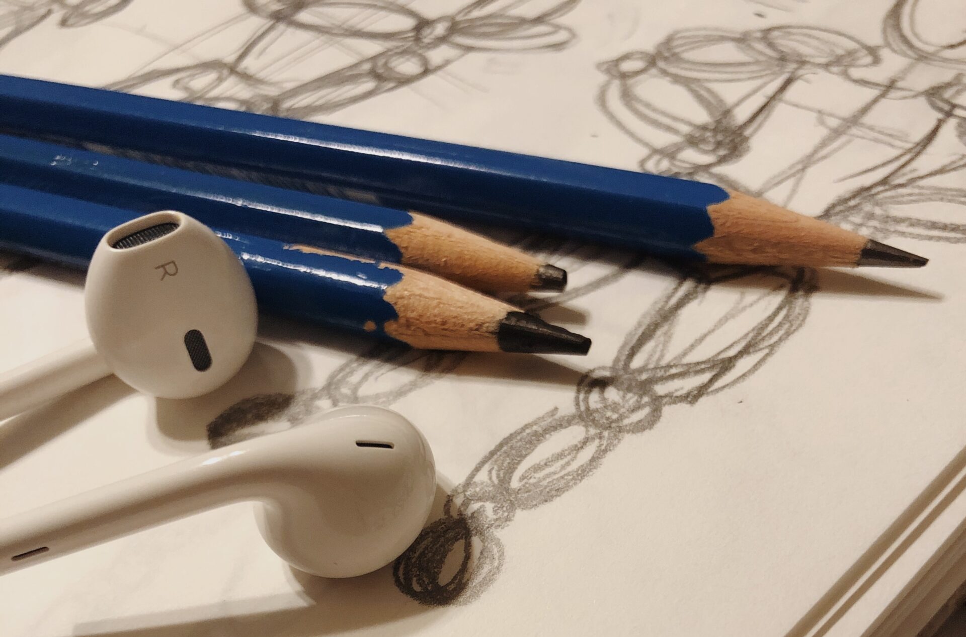 pencils and a pair of wired earbuds lay on a sketchbook page