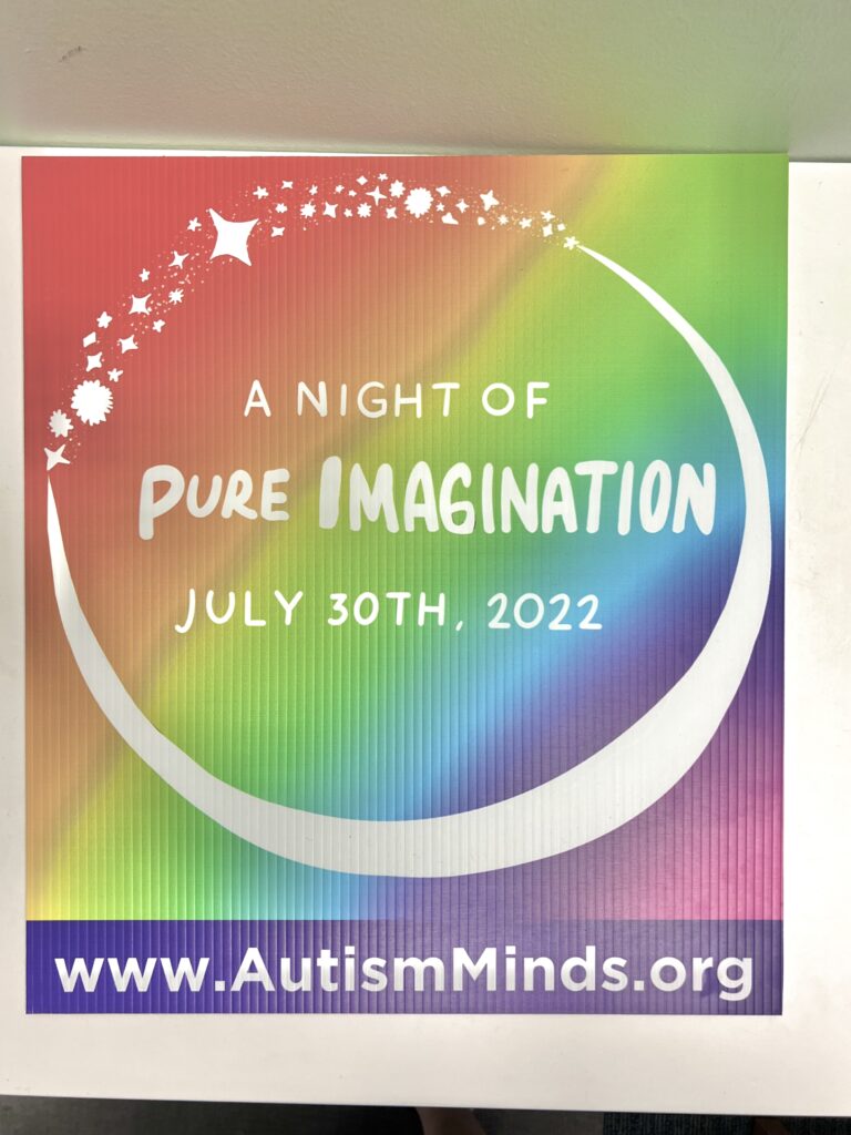 A square lawn sign with a rainbow gradient background, a white crescent moon with stars completing the circle frame white text that reads "A Night of Pure Imagination July 30th, 2022". A purple bar across the bottom of the sign says "www.Autism Minds.com" in white text.